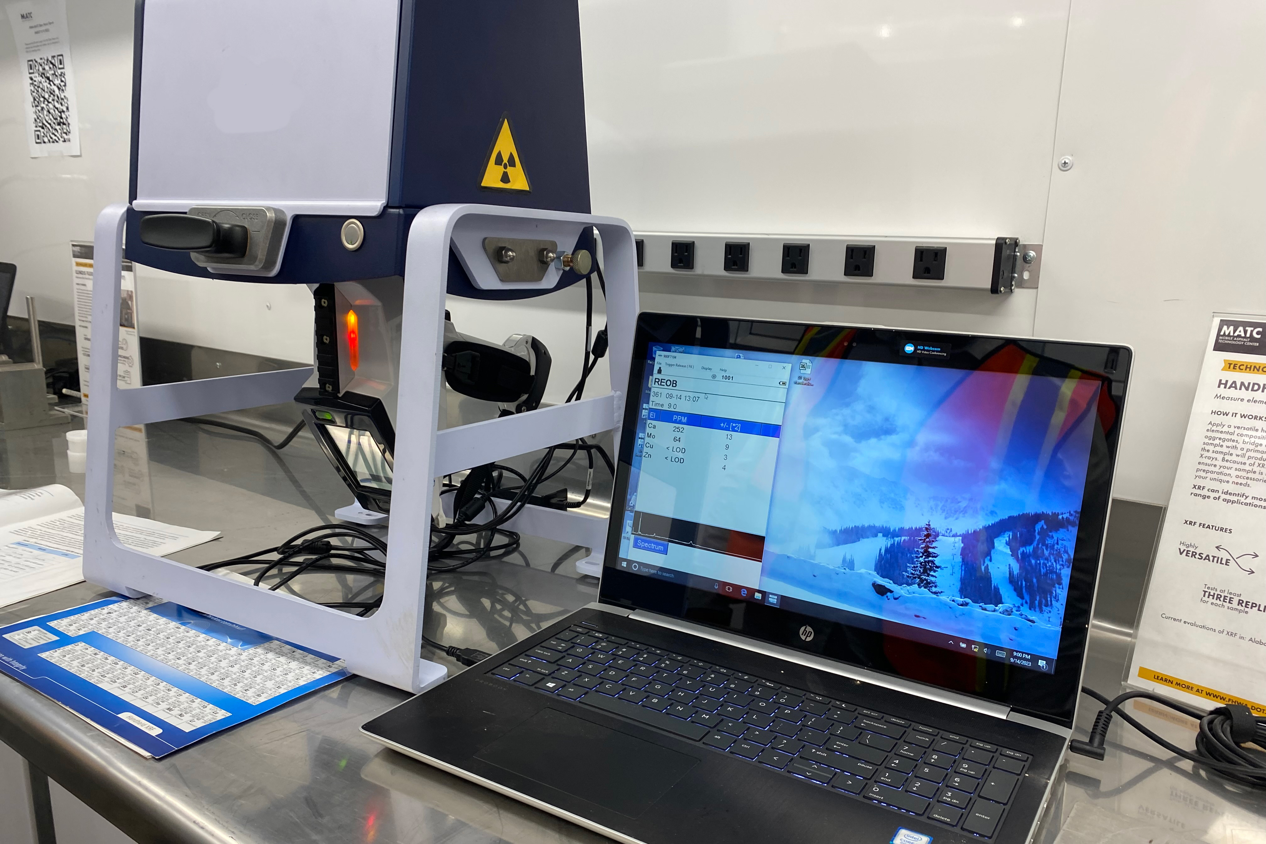 Set up of the x-ray reflectance test running, along with an accompanying laptop, on a small sample of asphalt binder in an asphalt laboratory